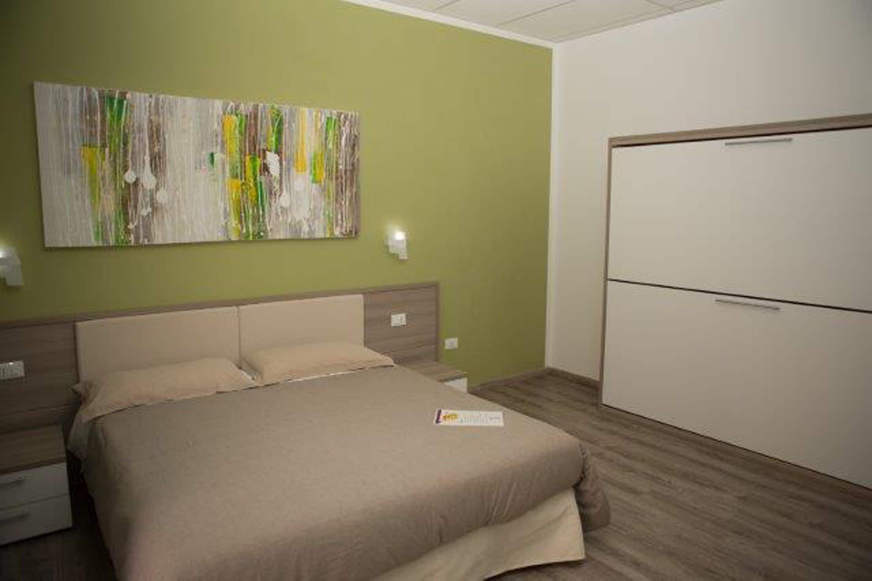 Ein Schlafzimmer mit Bett, Nachttisch, Kommode und einem Wandbild im abstrakten Stil.
