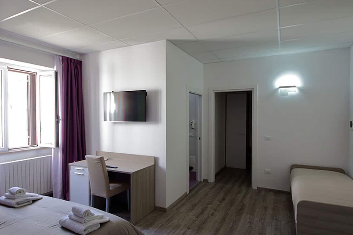 Una habitación de hotel con cama, escritorio, silla, televisor y puerta al baño.