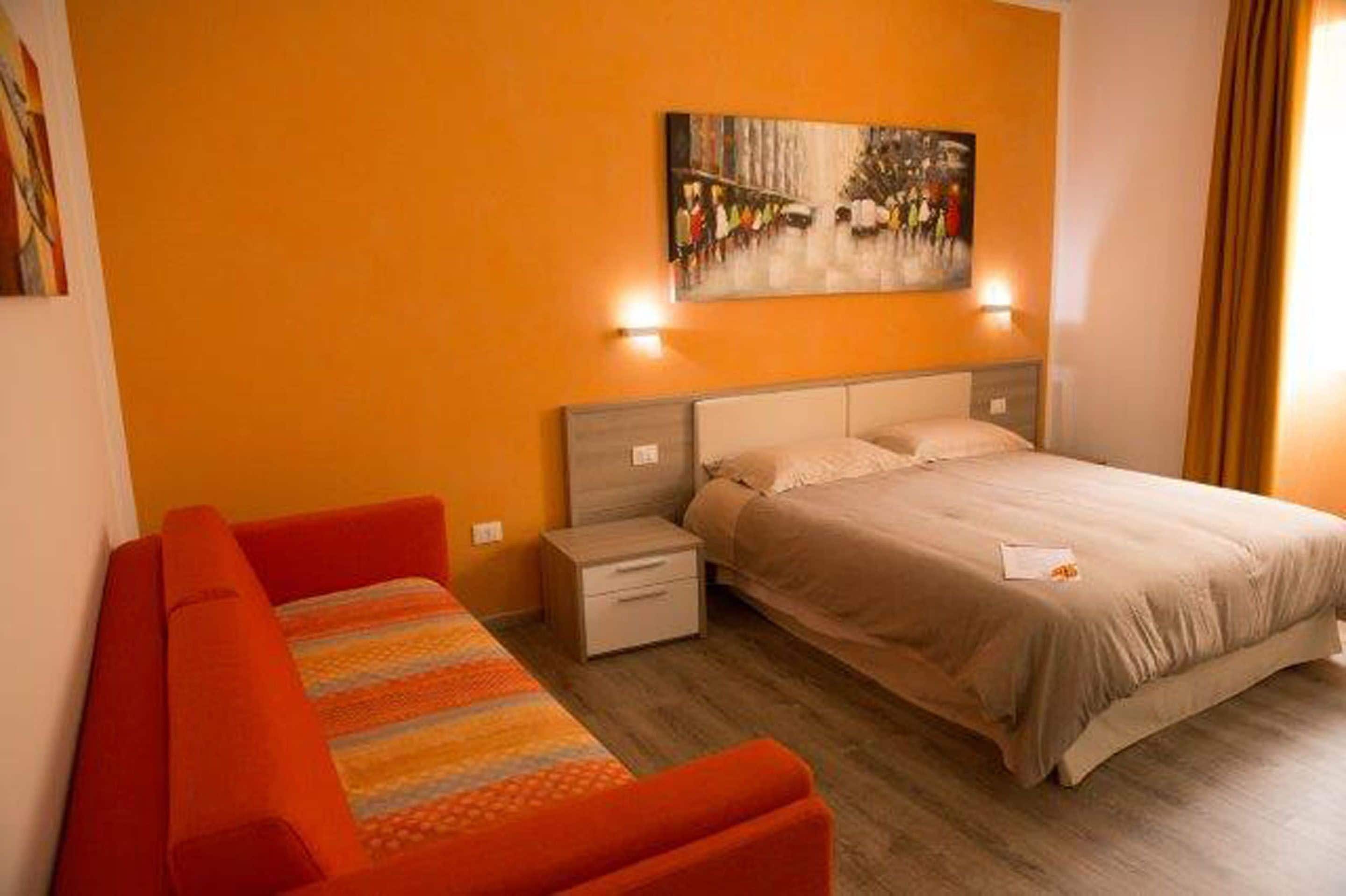 Una camera da letto con un letto, un comodino, un divano rosso e un quadro appeso al muro.
