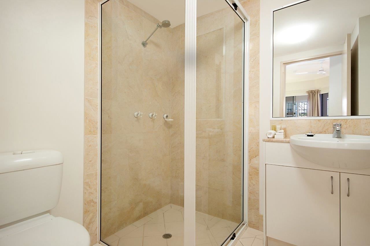 A modern bathroom with a glass-enclosed shower, a white toilet, and a sink with a mirror above it.