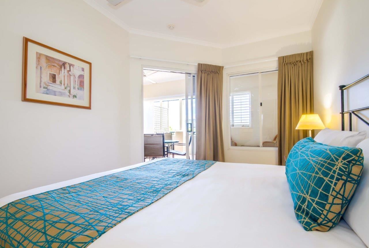 A hotel room with a bed, a window with curtains, a lamp, and a framed picture on the wall.