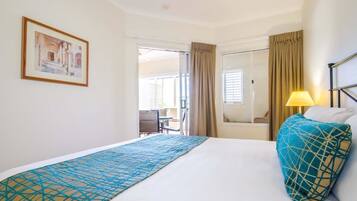 A hotel room with a bed, a window with curtains, a lamp, and a framed picture on the wall.