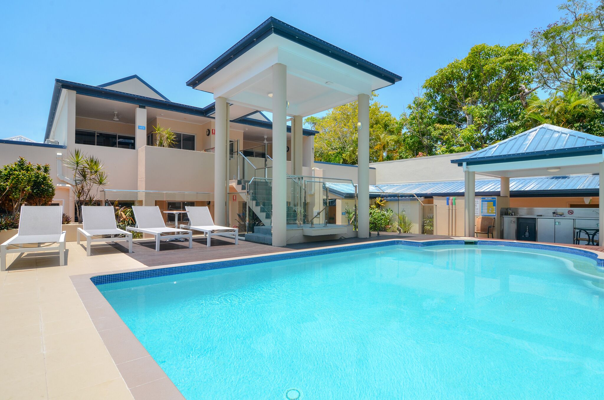 A swimming pool with lounge chairs and a covered area, surrounded by buildings and trees.