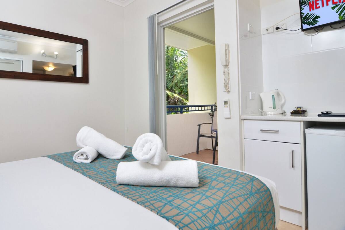A hotel room with a bed, a desk, a mirror, and a television.