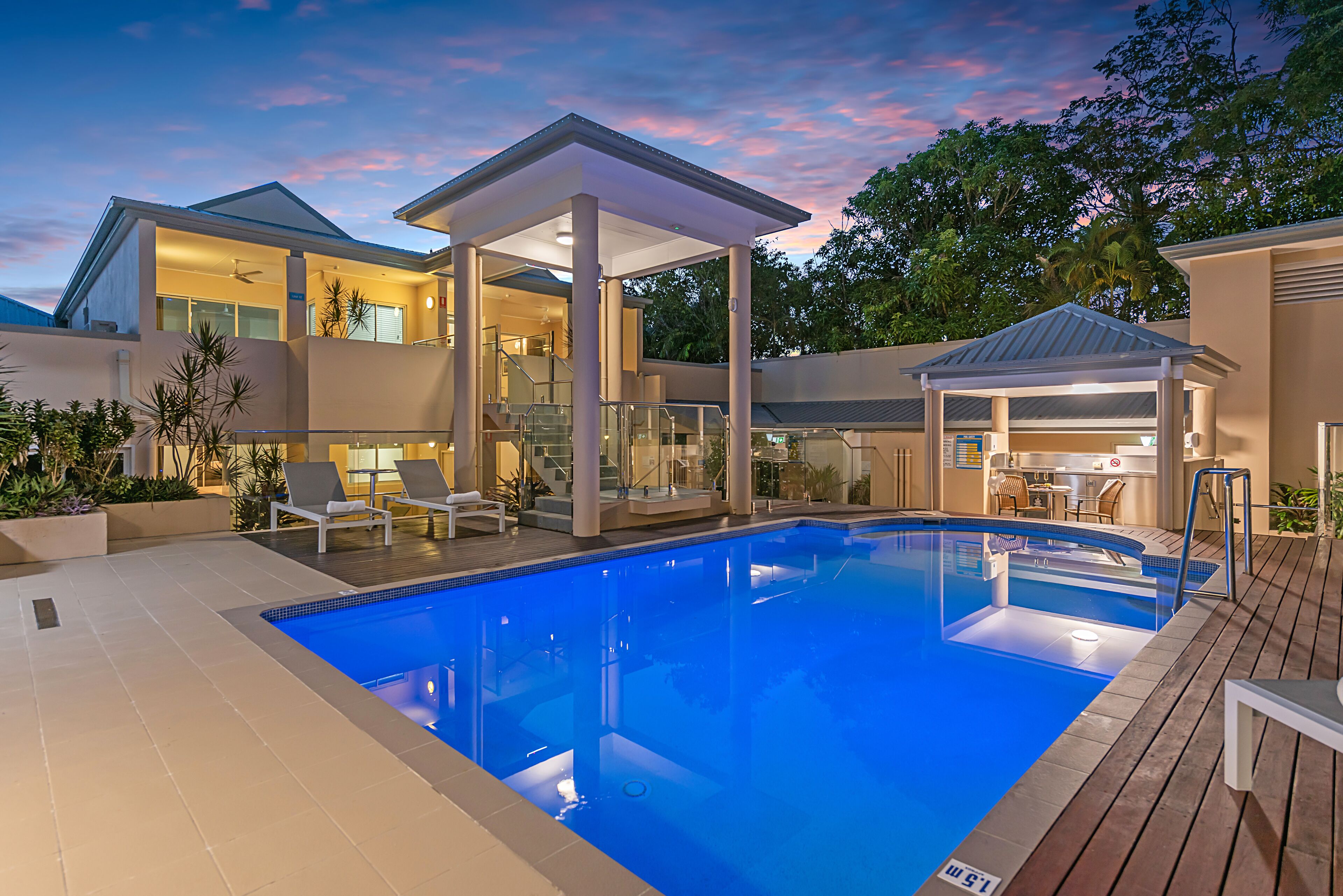 A modern pool area with a clear blue pool, lounge chairs, and a covered seating area.