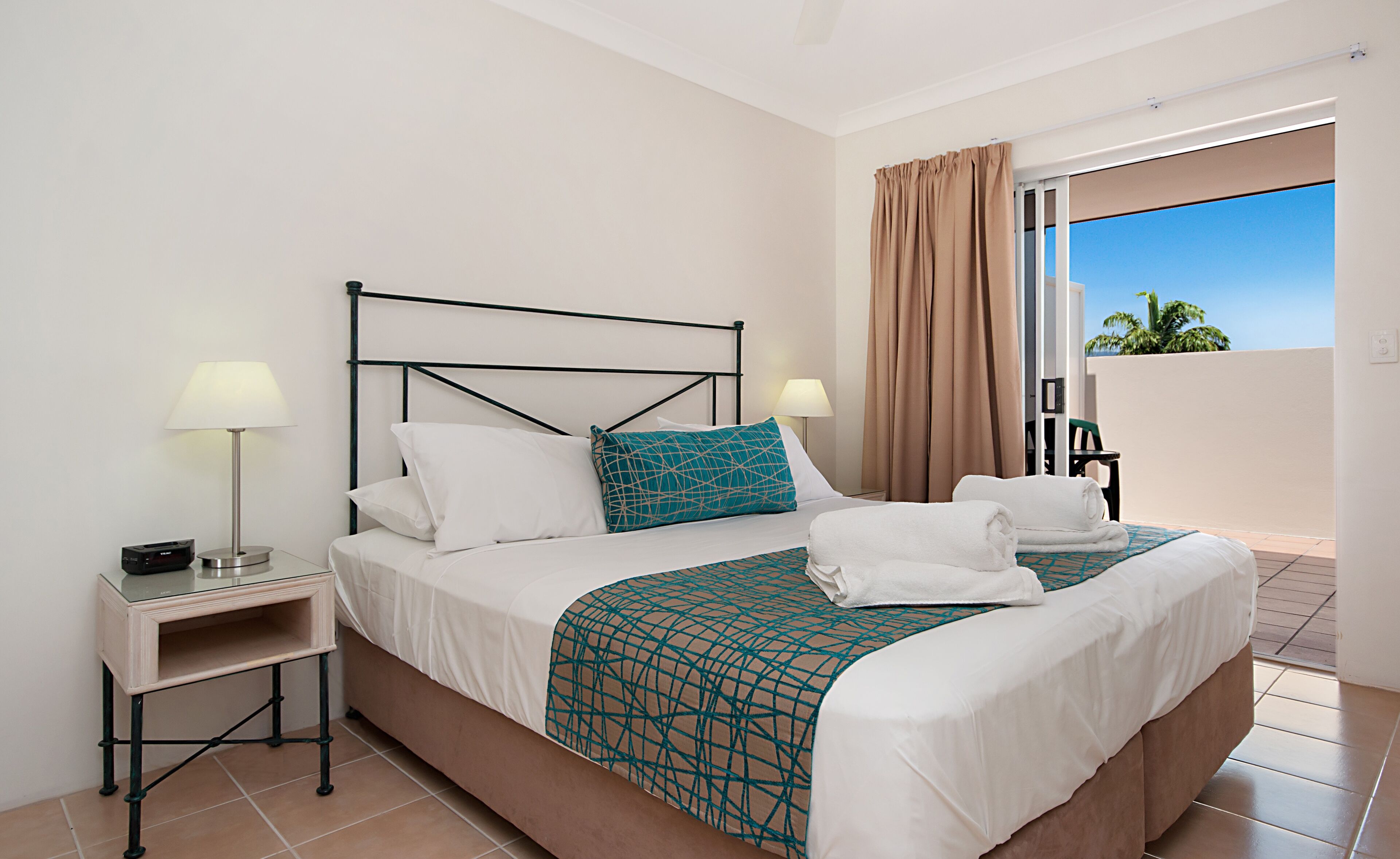 A hotel room with a bed, two bedside tables, a lamp, a window with curtains, and a view of the outdoors.