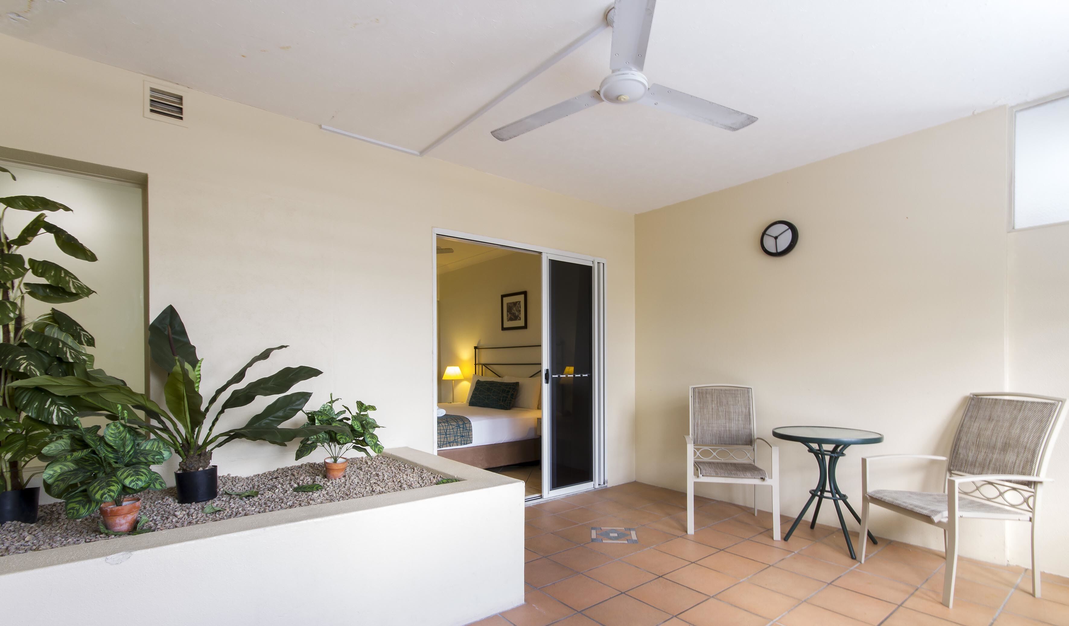 A hotel room with a bed, a chair, a table, and a ceiling fan.