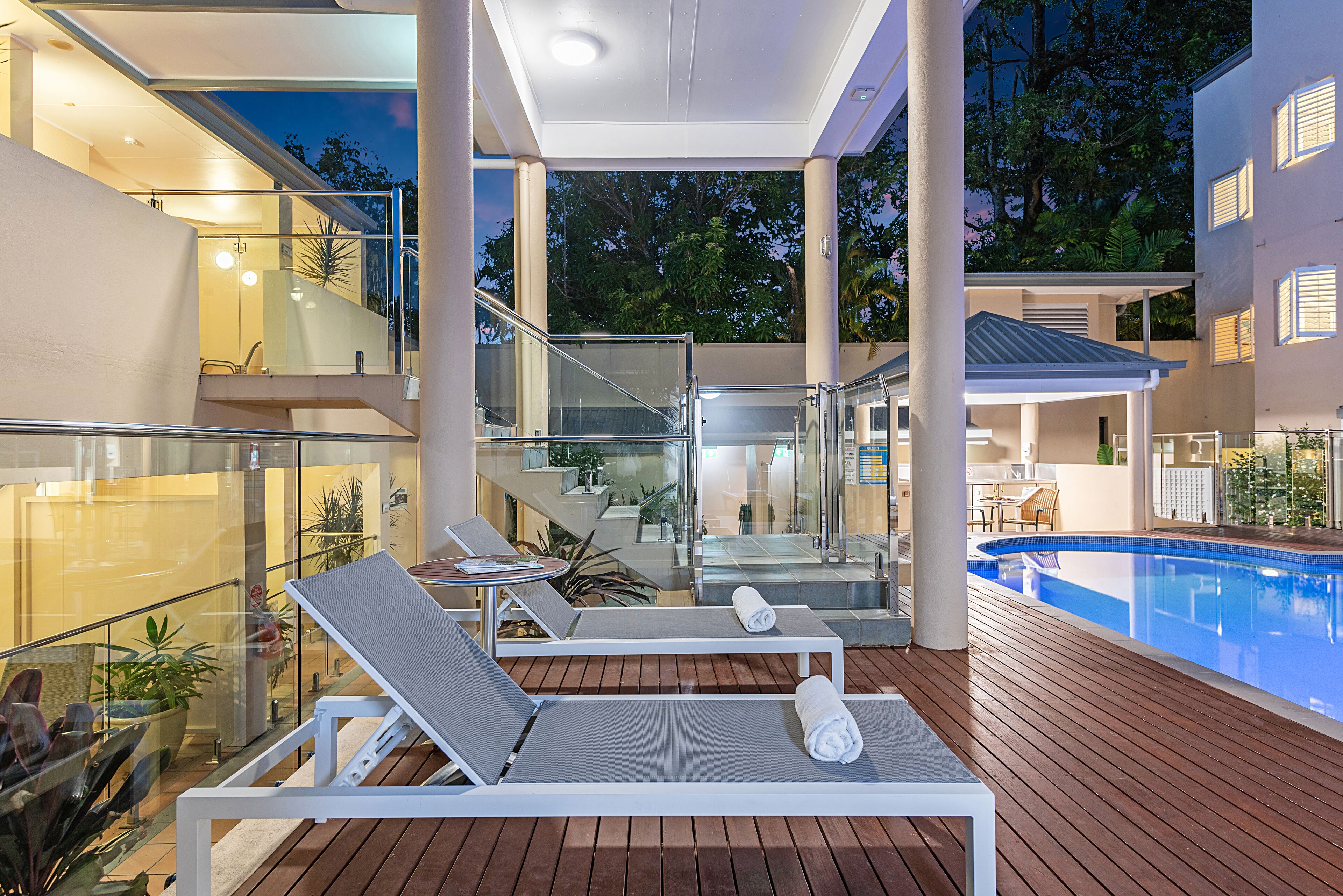 Un área de piscina moderna al aire libre con sillas de descanso y barandilla de vidrio.