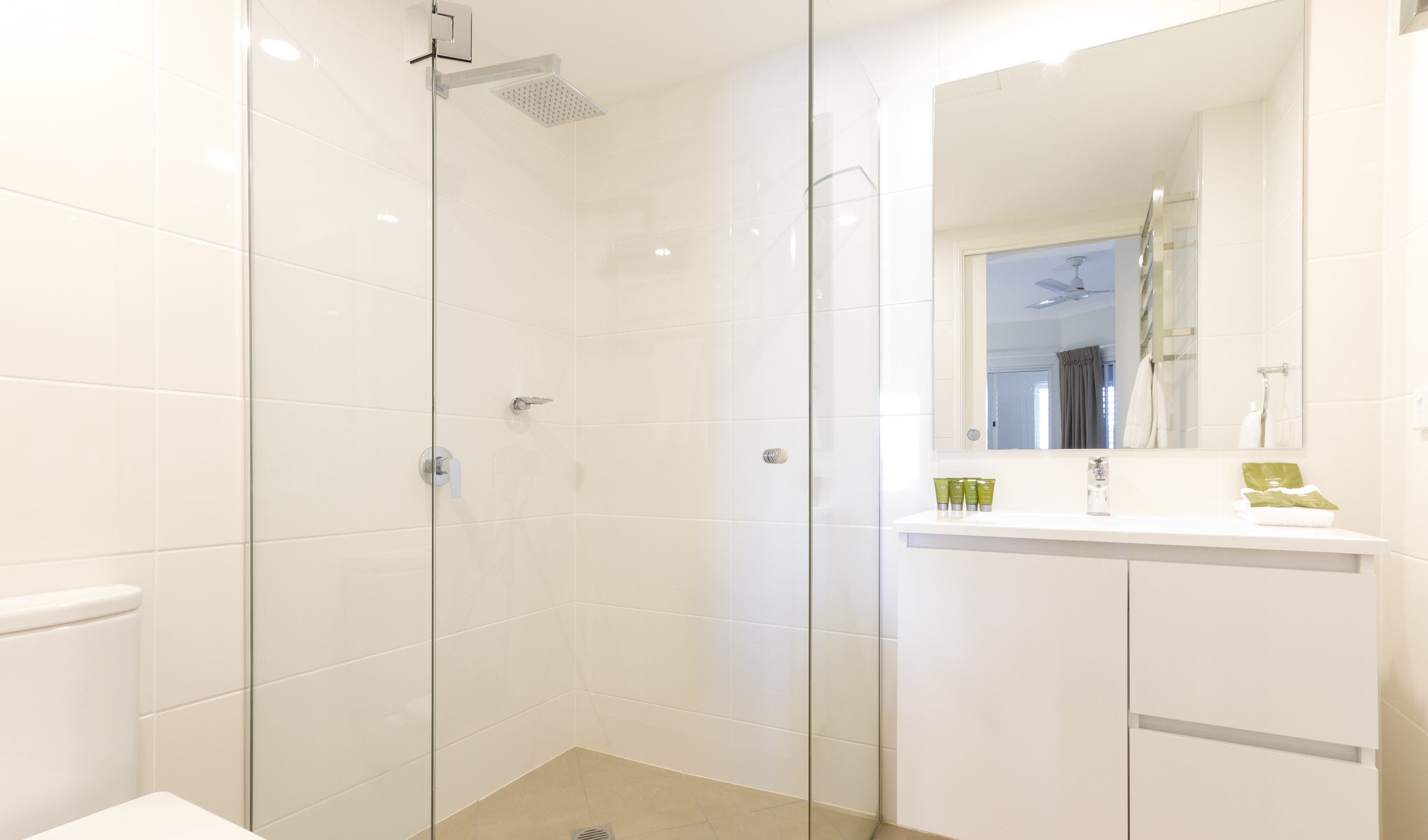 Ein modernes Badezimmer mit einer Duschkabine aus Glas, einem weißen Waschbecken mit Spiegel und Pflegeartikeln auf der Ablagefläche.