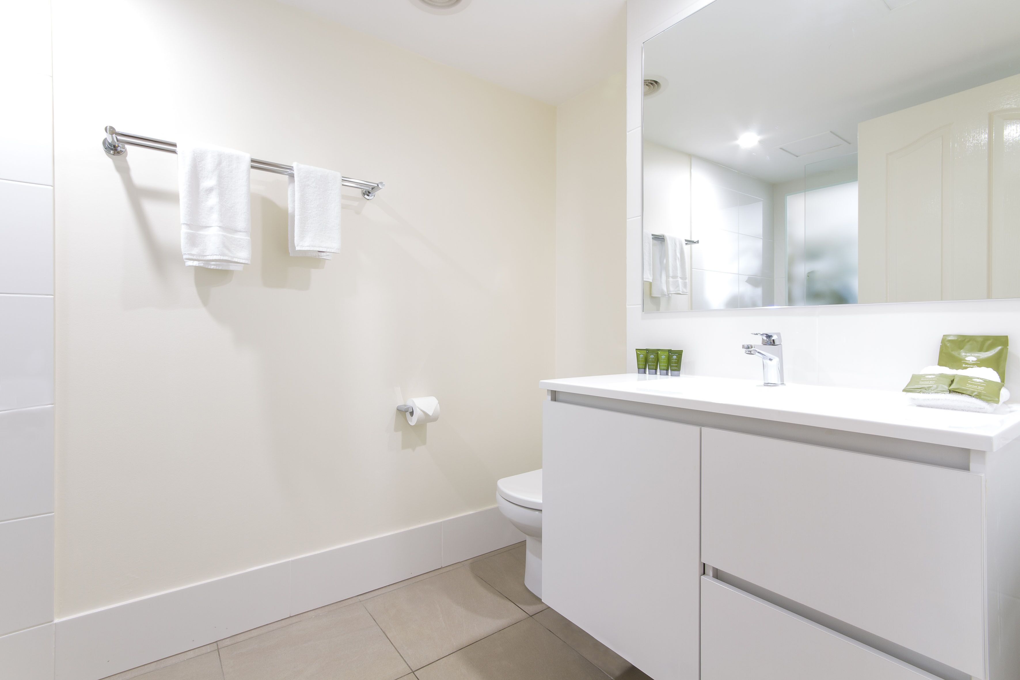 Un baño moderno con tocador blanco, un espejo grande y un perchero para toallas.