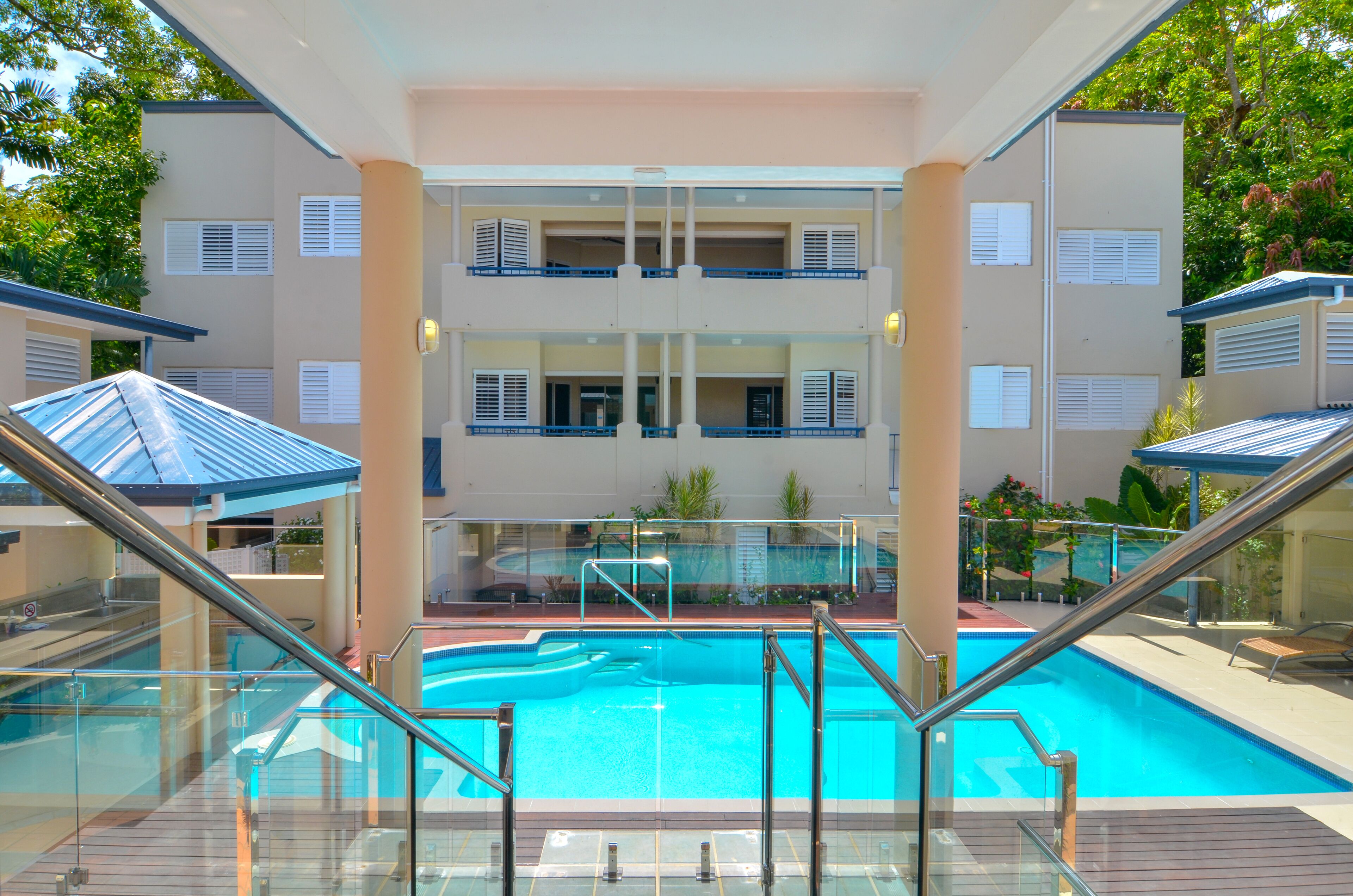 Una piscina con barandilla de vidrio, rodeada por un edificio con varios balcones y techo plano.