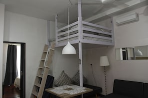 A bunk bed room with a ladder, a desk, a lamp, and a mirror.