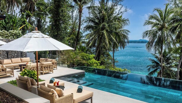 A poolside area with lounge chairs and an umbrella, overlooking a clear blue sea and palm trees. - Villa Analaya (Kamala)