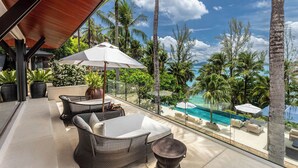 A balcony with wicker furniture, a white umbrella, and a view of a pool and palm trees. - Villa Analaya (Kamala)