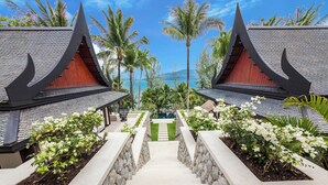 A symmetrical building with a central pathway leading to a pool, surrounded by tropical vegetation and palm trees. - Villa Analaya (Kamala)