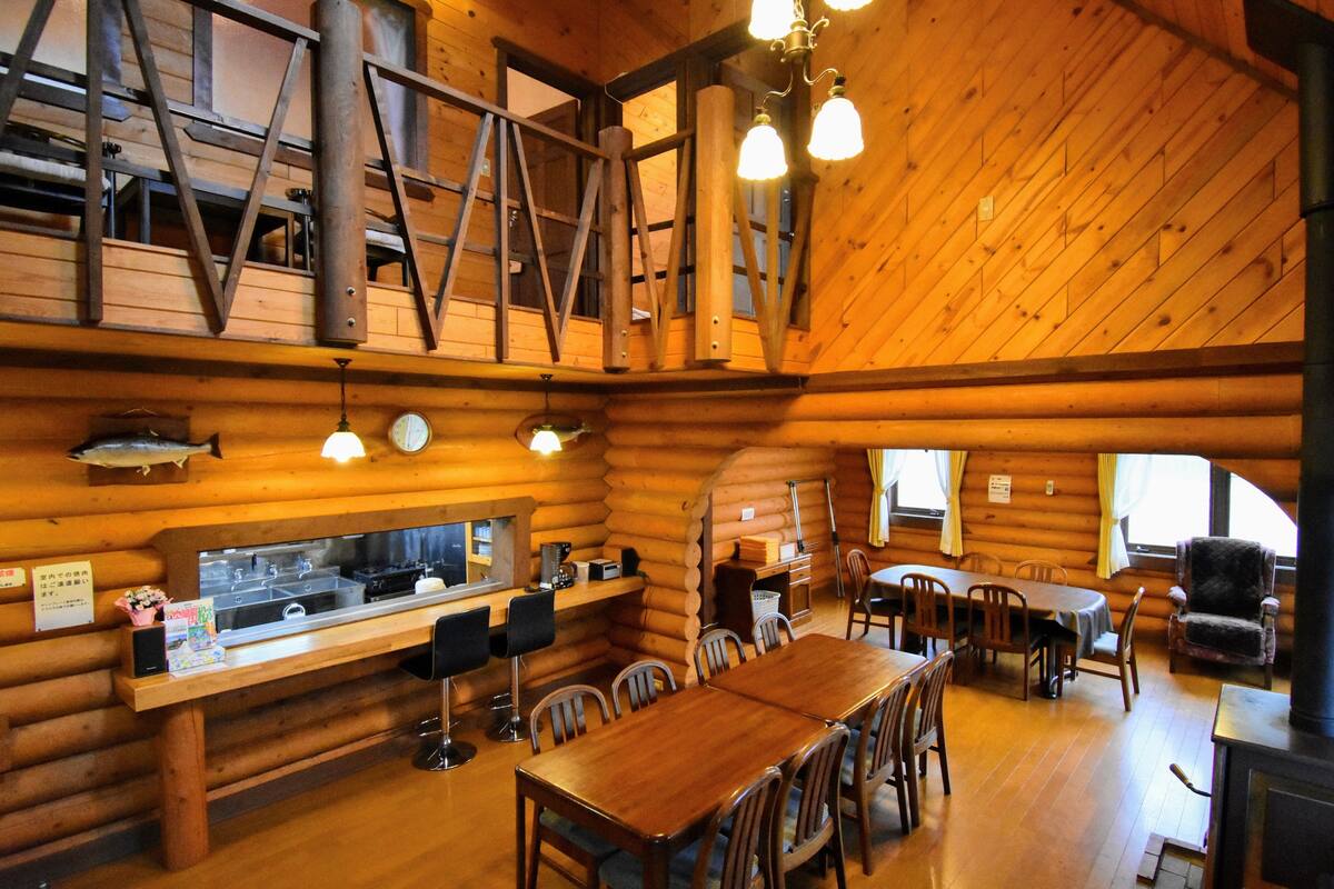 A log cabin interior with a dining area, kitchen, and a loft space with a ladder.