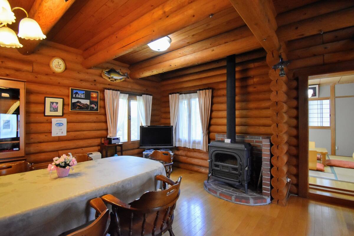 A log cabin interior with a dining area, fireplace, wooden walls, and a television.