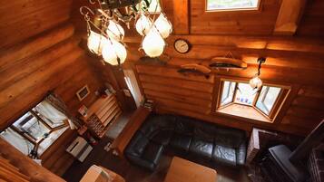 A cozy cabin interior with a wooden interior, a black leather sofa, a fireplace, and a clock on the wall.