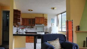 A compact kitchen with wooden cabinets, a central island, and a dining area with a blue chair. - Mayra's Spanish School (Baños de Agua Santa)