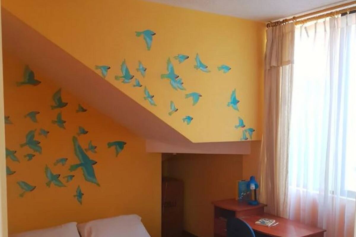 Een slaapkamer met een bed, een bureau en een raam met gordijnen.