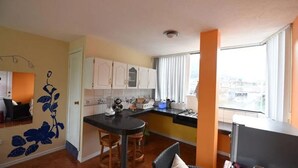 A compact kitchen with white cabinets, a black countertop, and a window providing a city view. - Mayra's Spanish School (Baños de Agua Santa)
