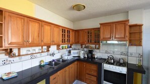 A kitchen with wooden cabinets, a black countertop, a stove, and a microwave. - Mayra's Spanish School (Baños de Agua Santa)