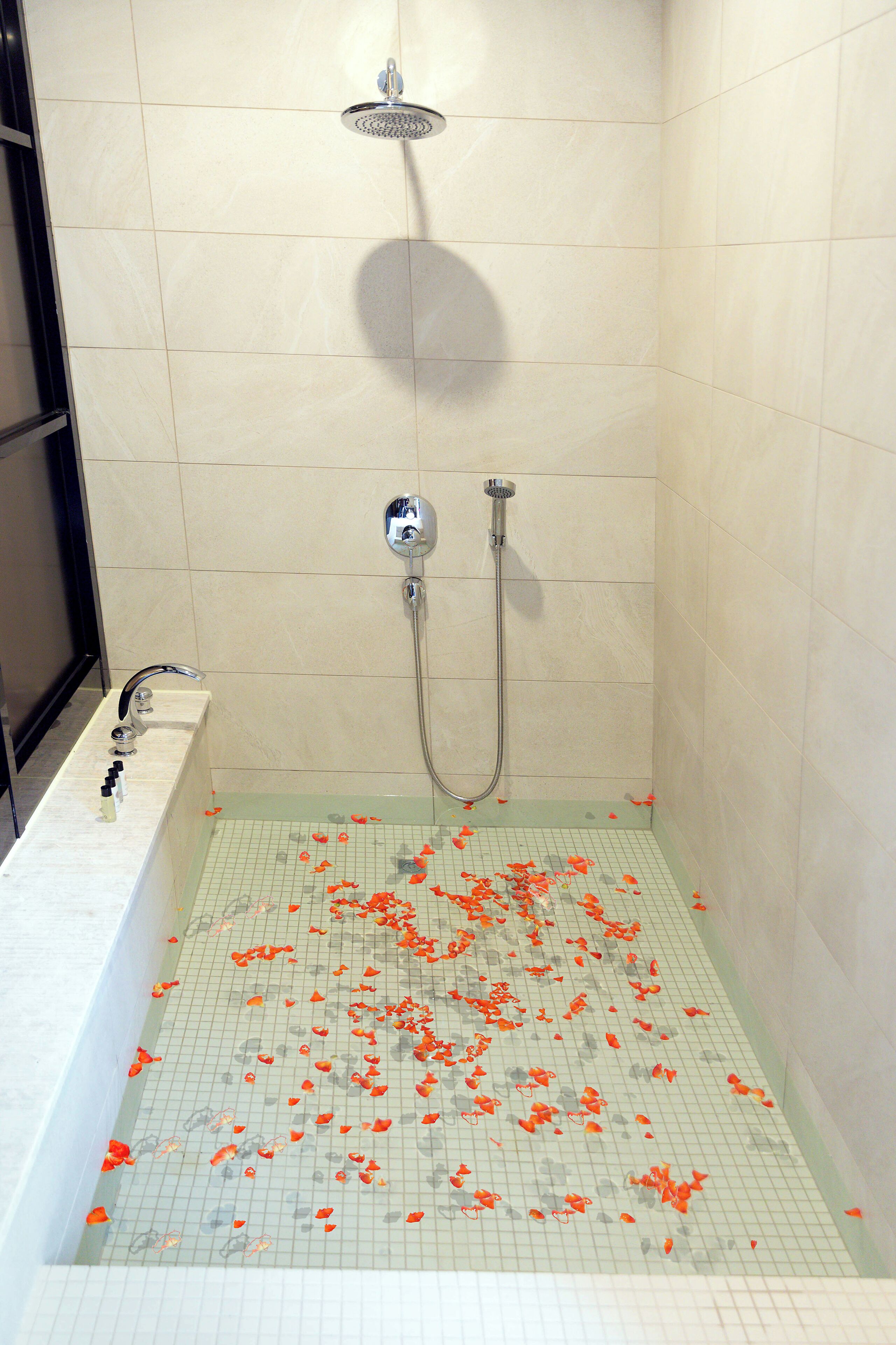 A shower with a grid floor, a handheld showerhead, and a wall-mounted faucet.