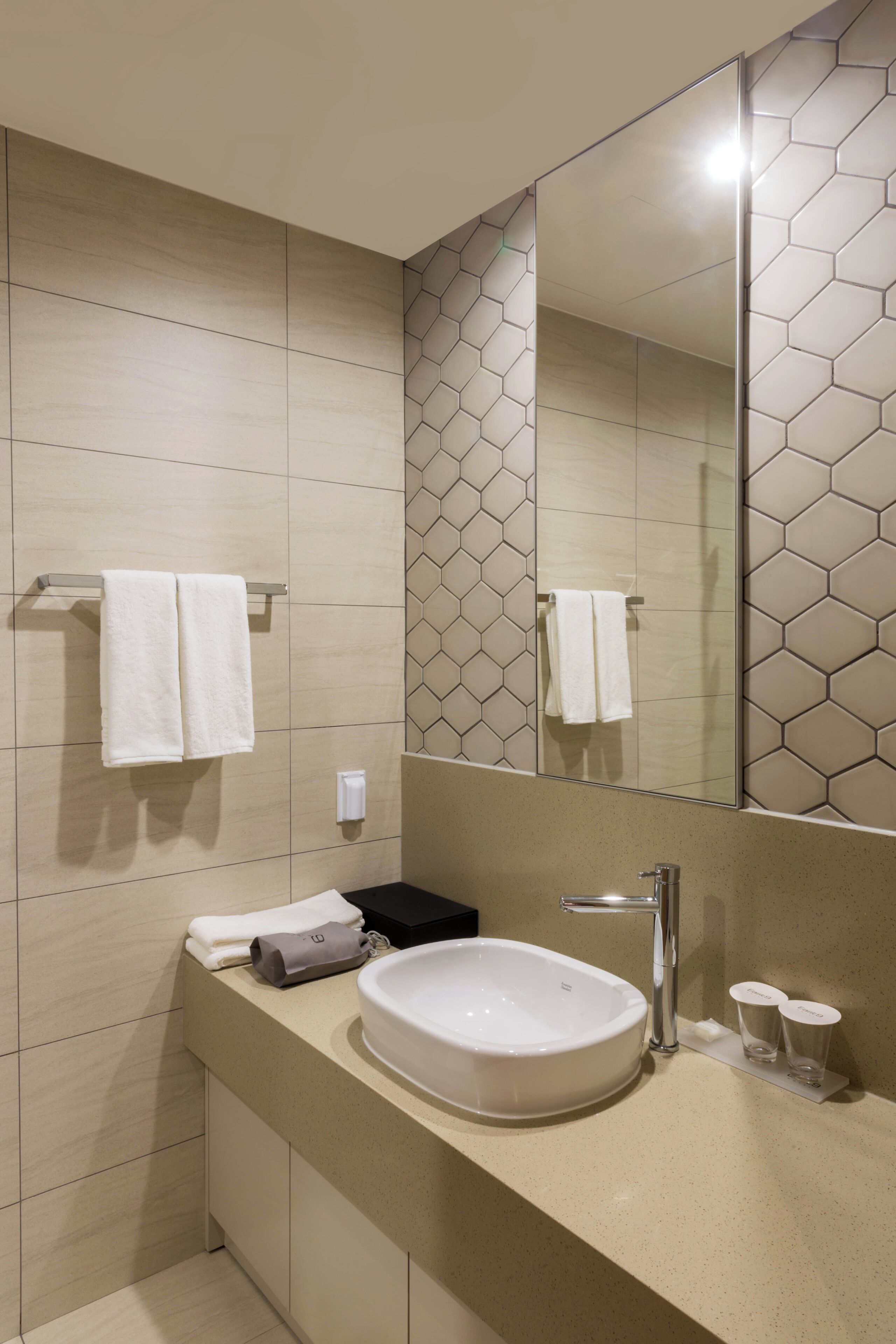 Un baño moderno con un espejo grande, un lavamanos blanco y un perchero para toallas.
