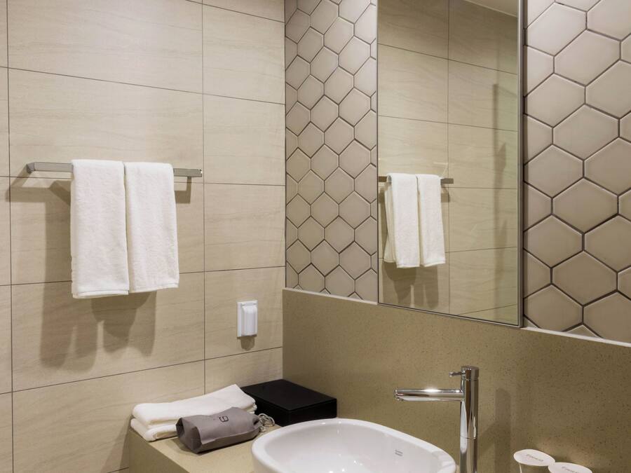 Un baño moderno con un espejo grande, un lavamanos blanco y un perchero para toallas.