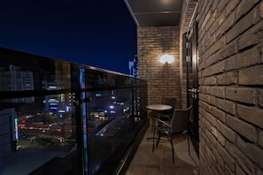 A balcony with a glass railing, a brick wall, and a table with chairs. - Hotel EAST9 (Gangneung)