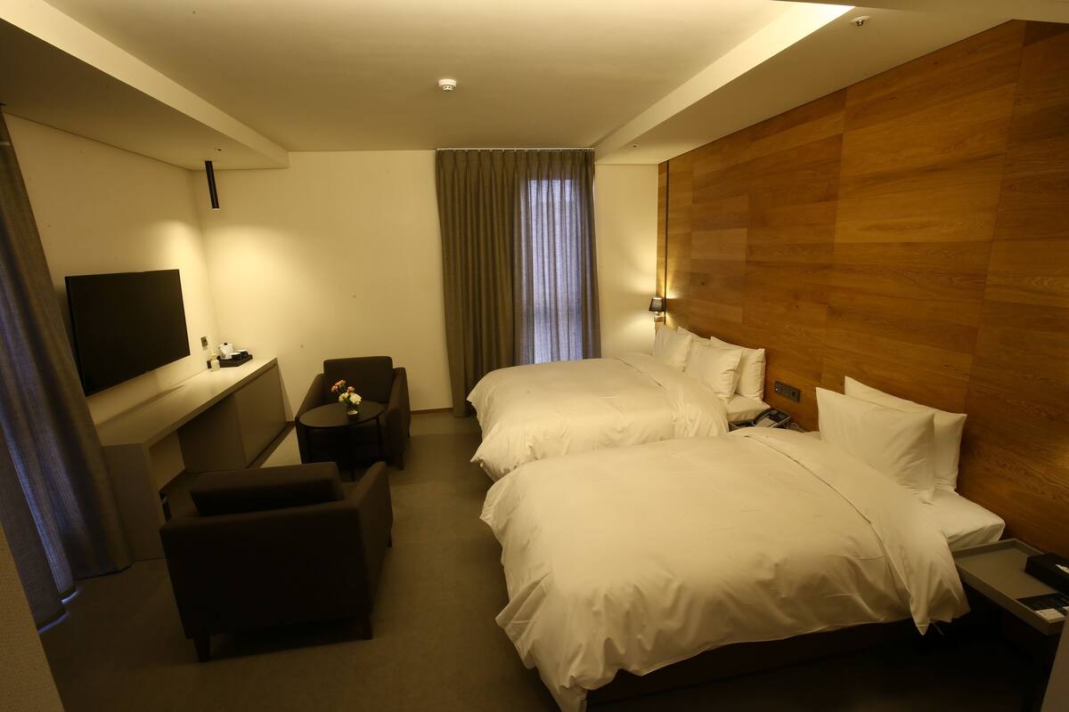 Quarto de hotel com duas camas, televisão, escrivaninha e uma cadeira.