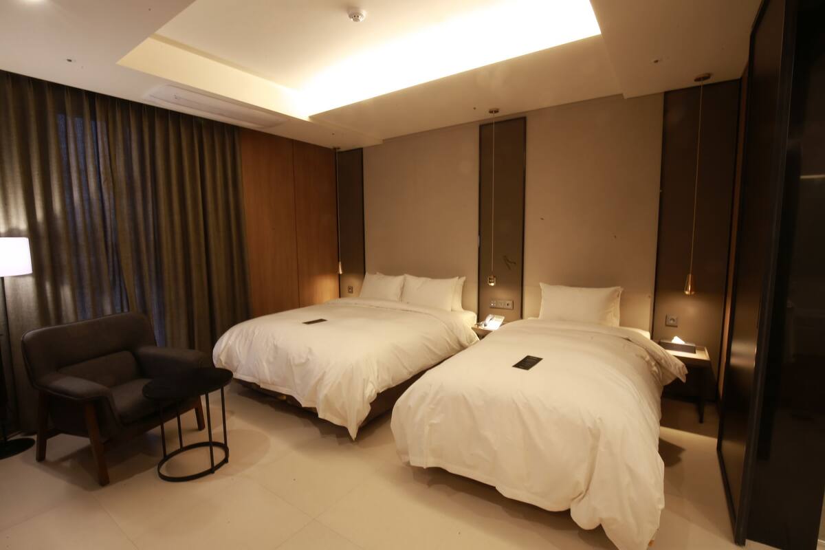 Quarto de hotel moderno com duas camas, uma mesa e uma cadeira.