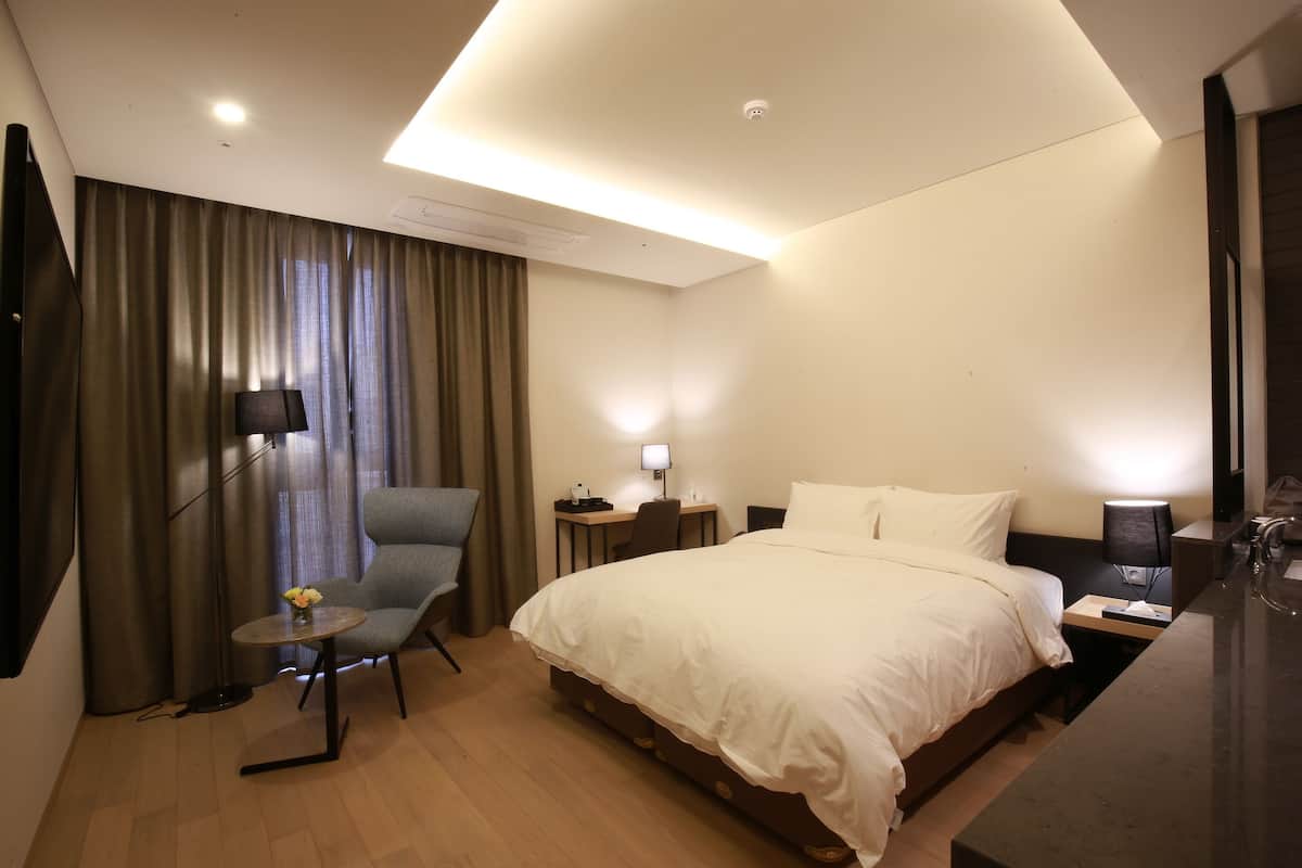 Quarto de hotel moderno com uma cama grande, uma escrivaninha com cadeira, uma mesinha com flores e uma televisão na parede.