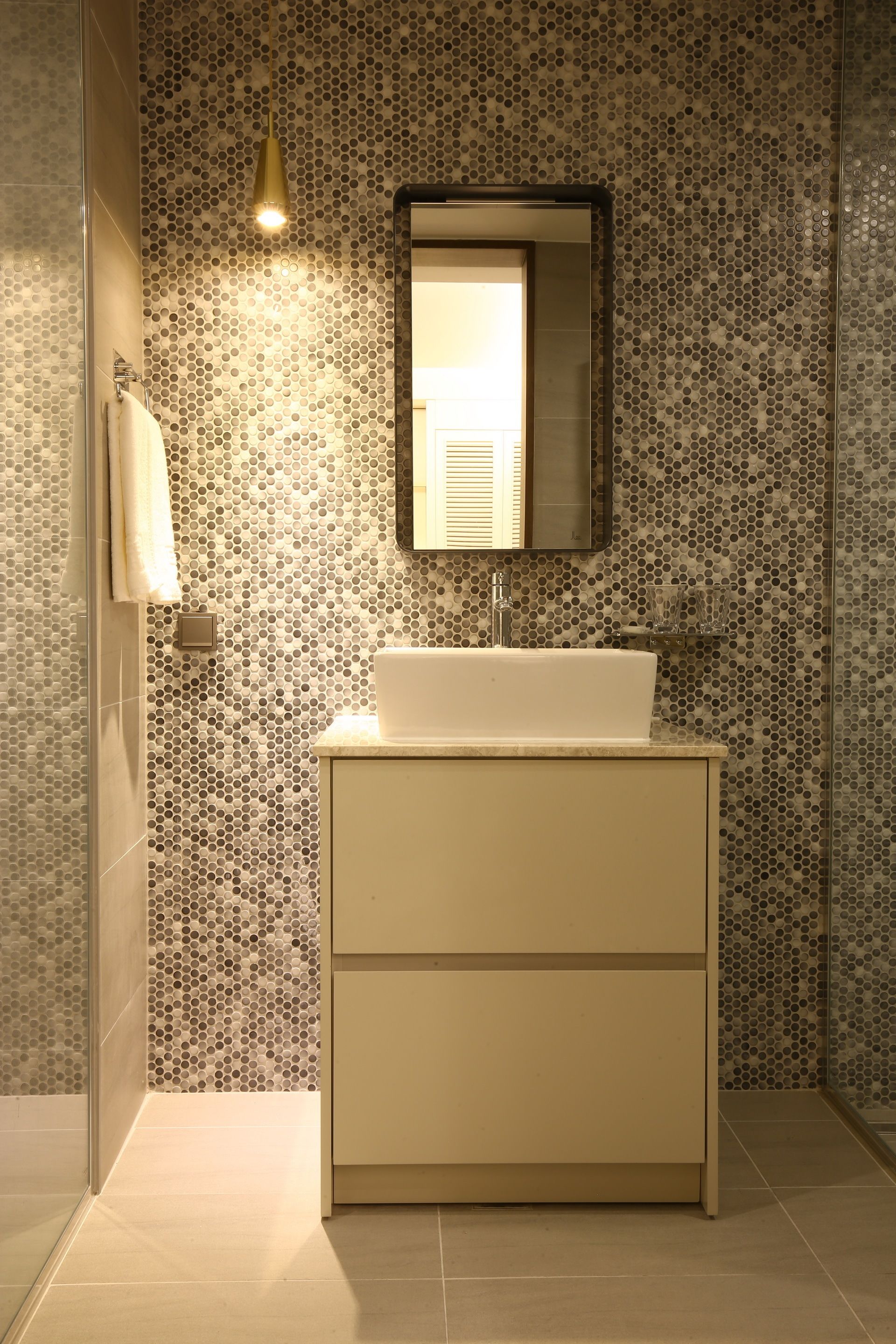 A bathroom with a white sink, a mirror, and a tiled wall with a circular pattern.