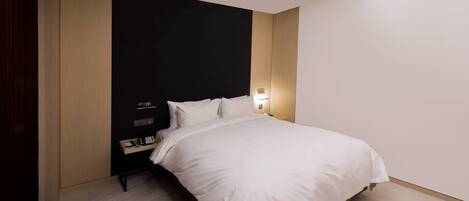 A modern hotel room with a large bed, a bedside table, a nightstand, and a wall-mounted light.