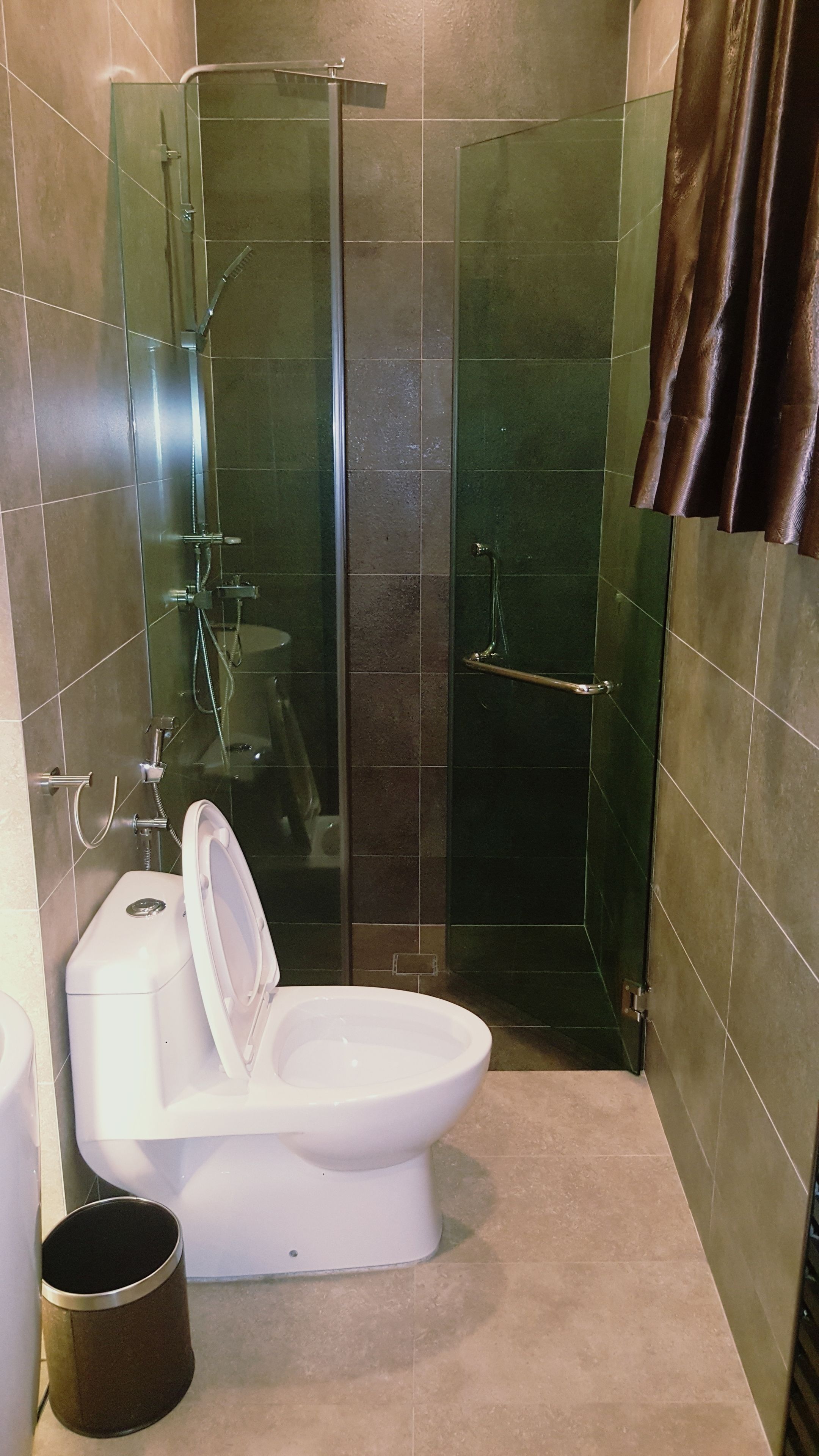 Een badkamer met een douchecabine van glas, een toilet en een prullenbak.