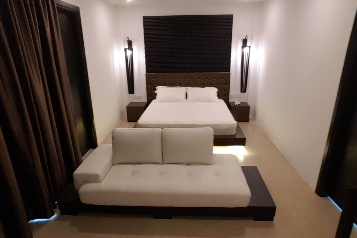 Een moderne hotelkamer met een groot bed, een bank, twee nachtkastjes en een wandlamp.