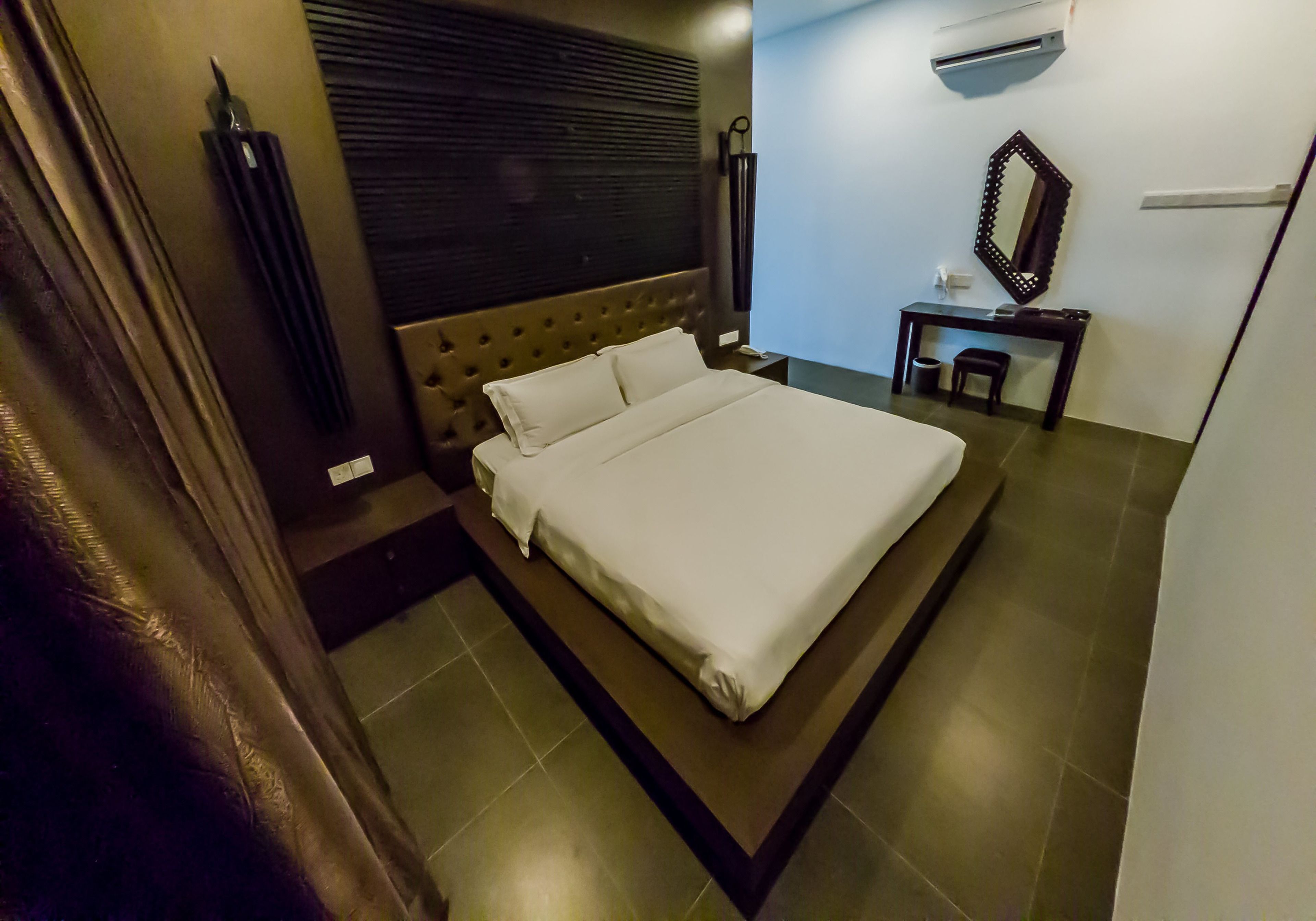 A neatly made bed with a headboard, a small bedside table, a mirror, and an air conditioning unit on the wall.
