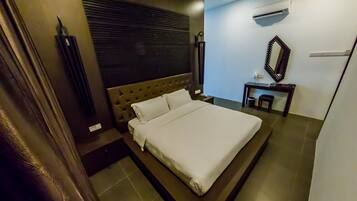 A neatly made bed with a headboard, a small bedside table, a mirror, and an air conditioning unit on the wall.