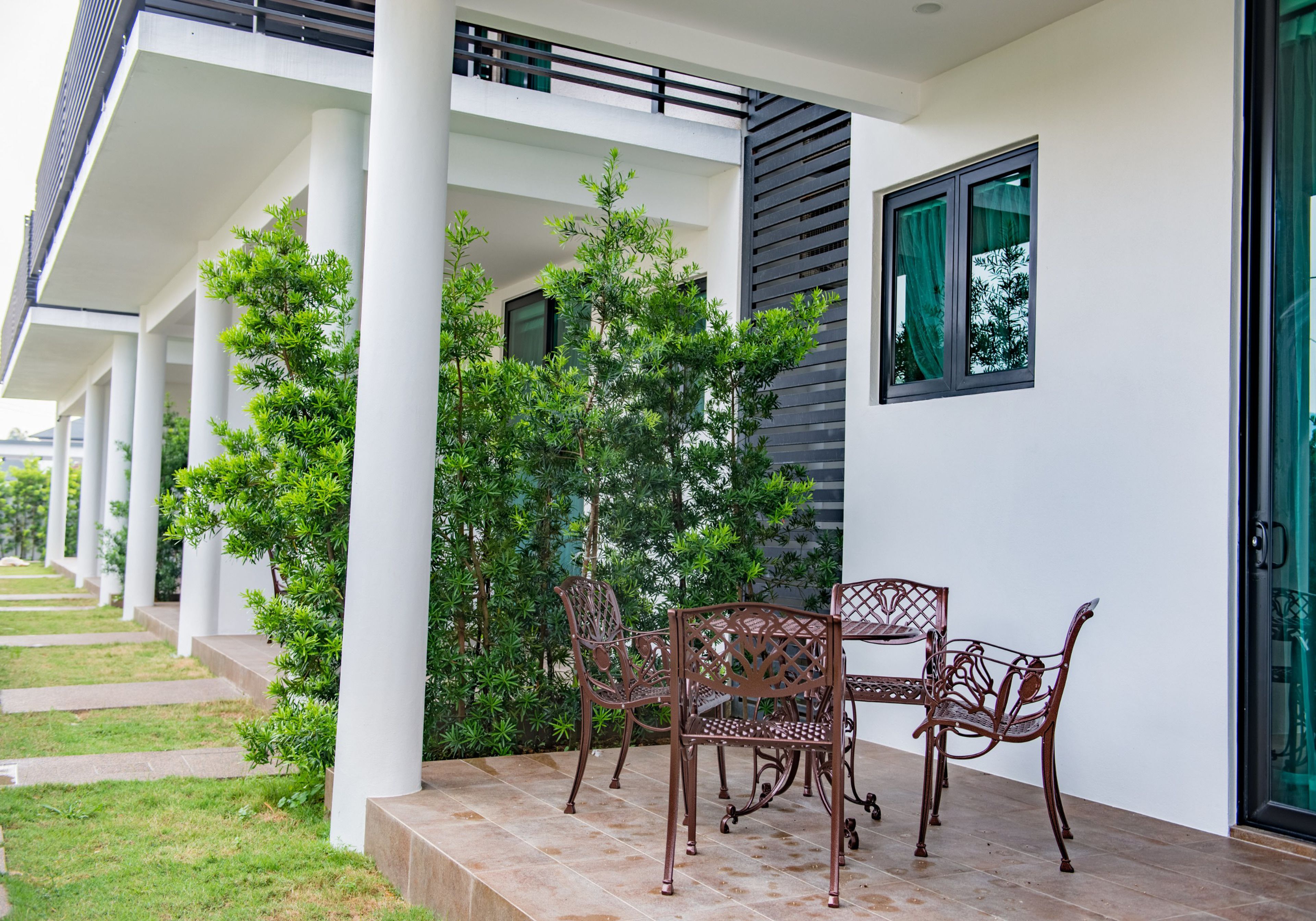 Un área de estar moderna al aire libre, con una mesa y sillas, rodeada de follaje y columnas blancas.