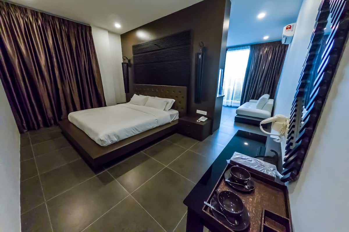 Een moderne hotelkamer met een groot bed, een nachtkastje met een telefoon, en een klein zithoekje met een stoel en een tafeltje.