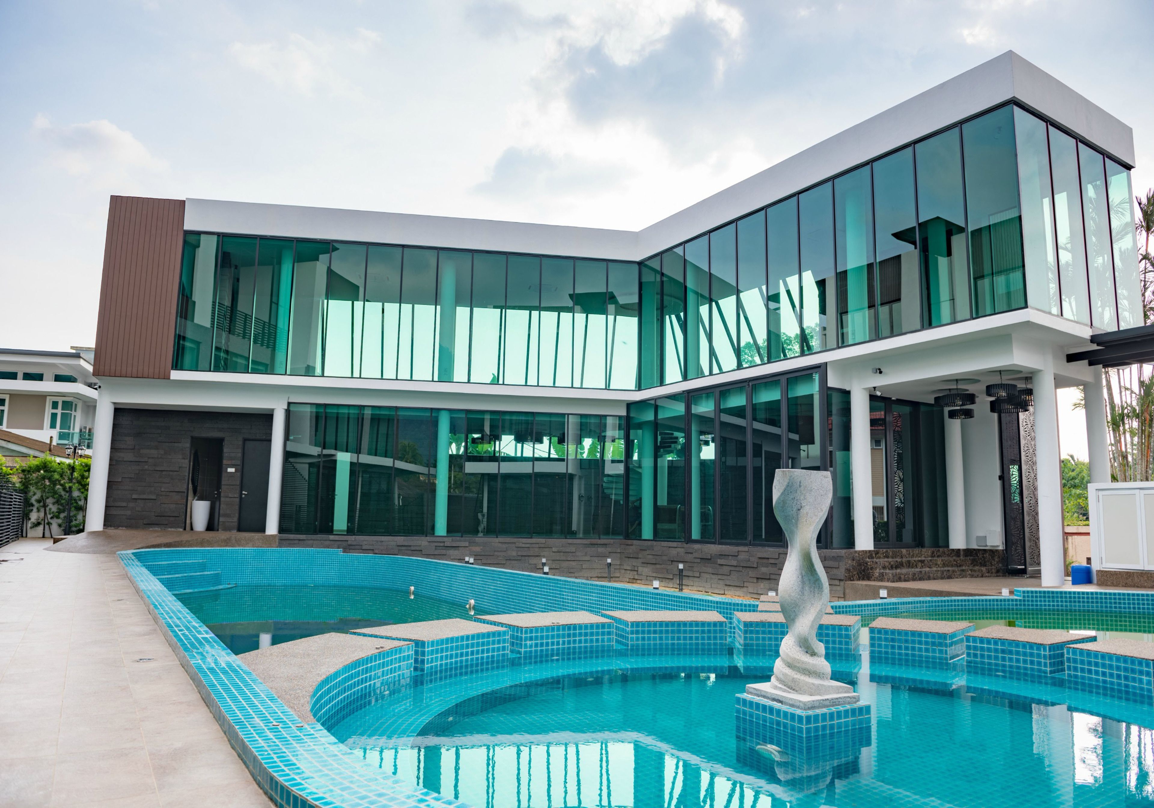 A modern building with a large glass facade, a swimming pool with blue tiles, and a unique sculpture in the pool.