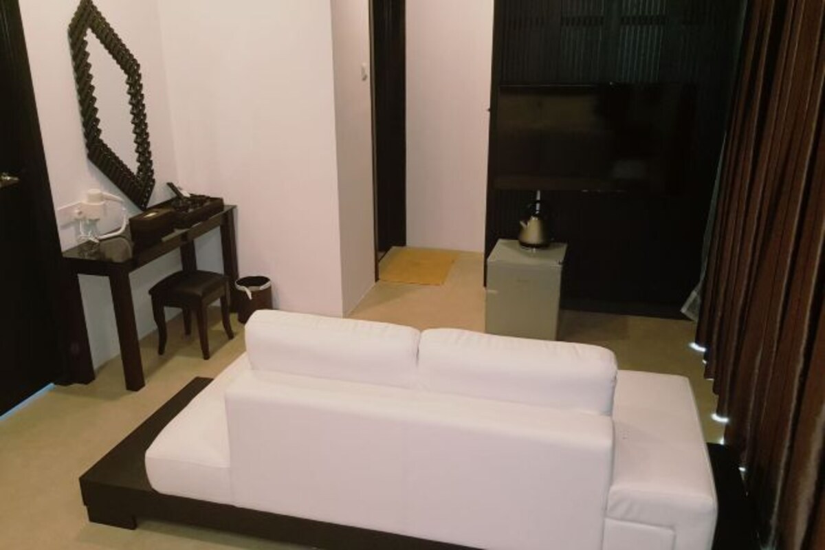 Ein weißes Sofa in einem Raum mit einem Holznachttisch, einem Spiegel und einem kleinen Tisch mit einer Flasche.