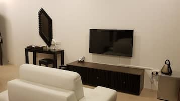 A modern living room with a flat-screen TV mounted on the wall, a white sofa, a dark wooden coffee table, and a small cabinet with a kettle.