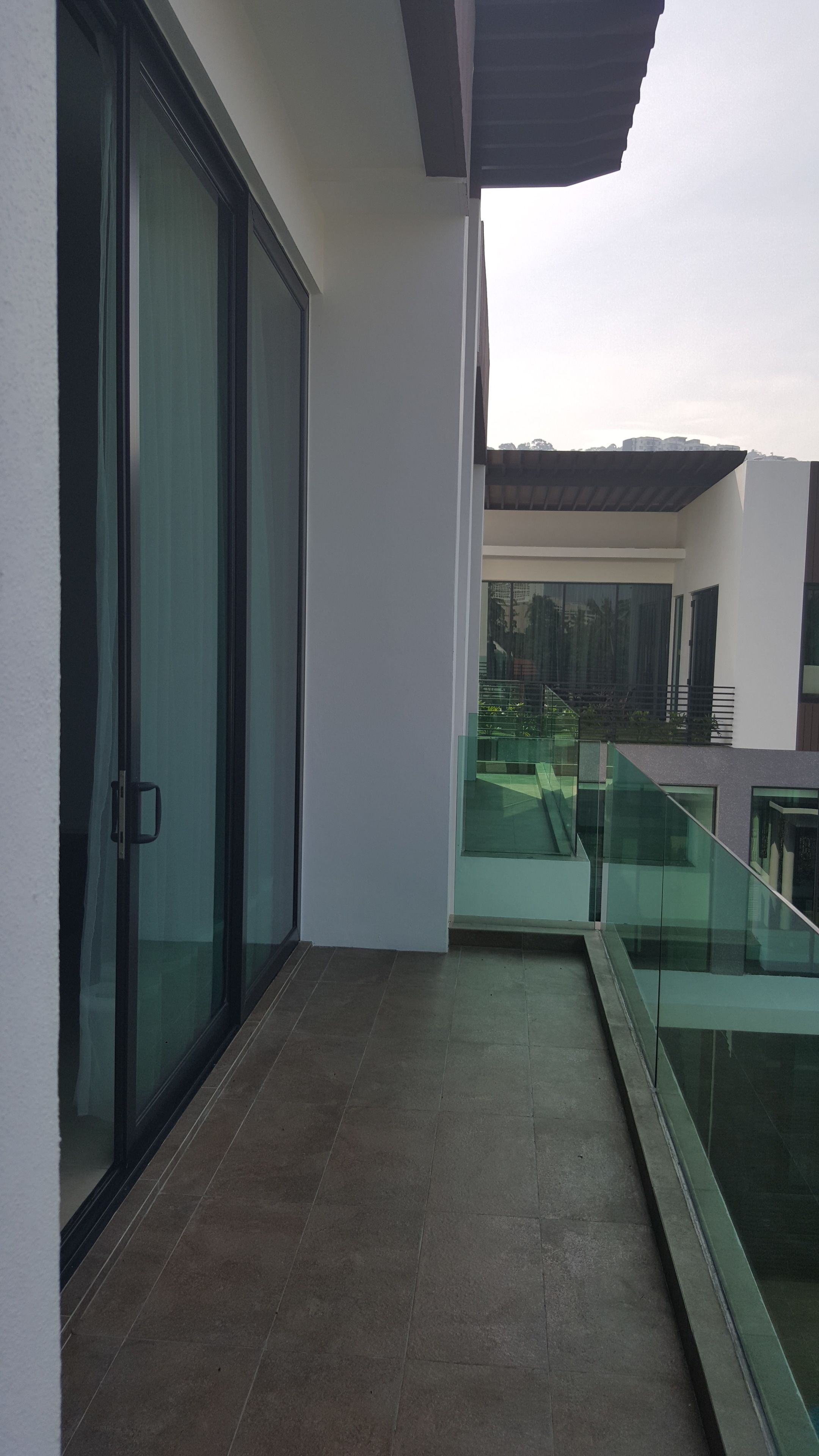 A balcony with glass railings, a sliding glass door, and a tiled floor.