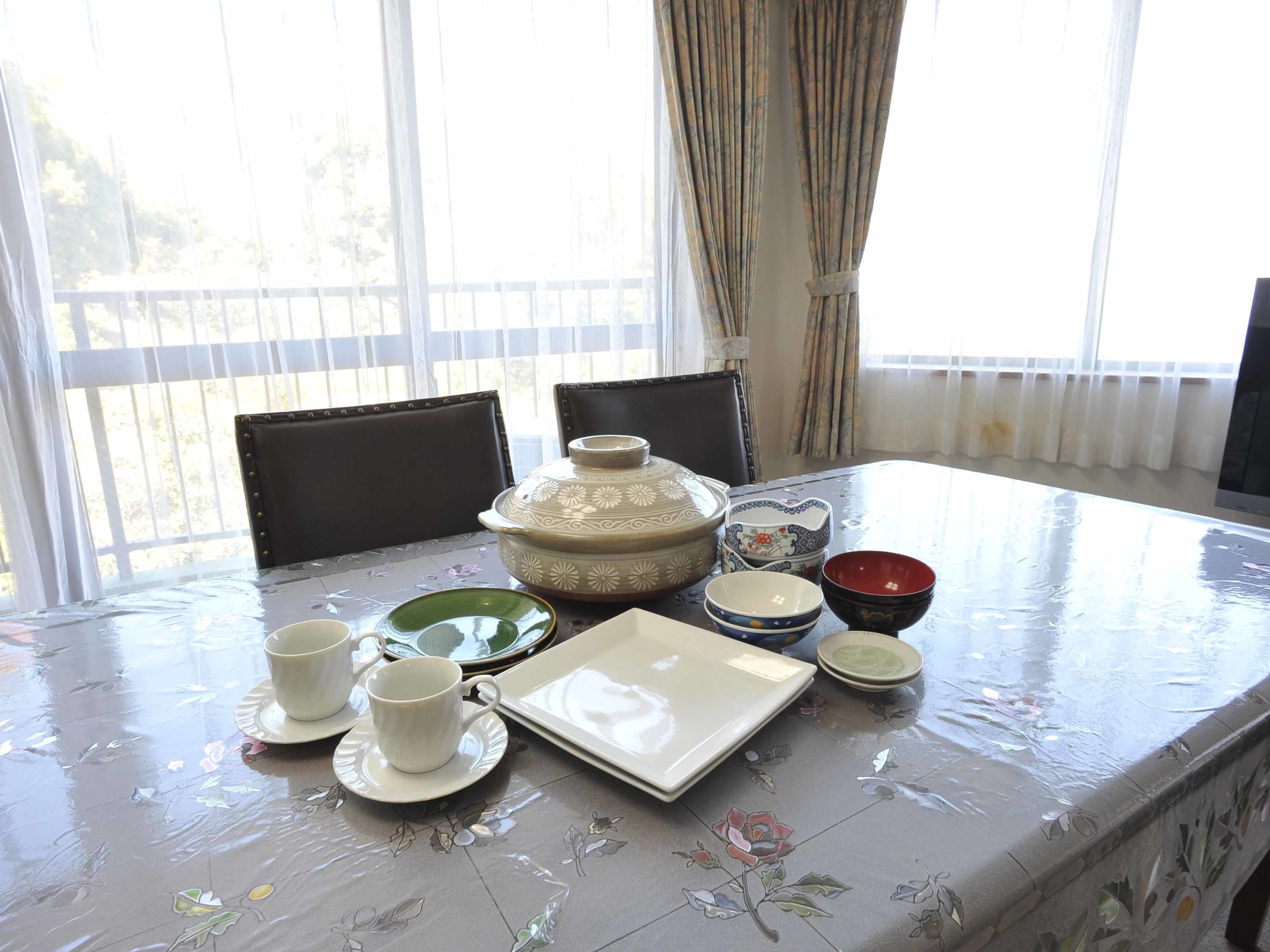 A dining table with a floral tablecloth, a large decorative pot, and various bowls and plates.