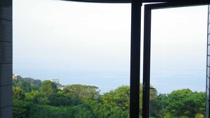 Ein Zimmer mit einem großen Panoramafenster, das einen Blick auf eine üppige grüne Landschaft und entfernte Gebäude freigibt.