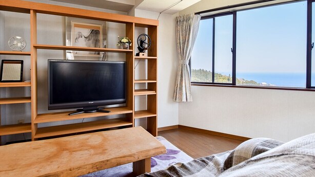 Ein modernes Wohnzimmer mit Fernseher, Holzregalen und einem großen Fenster mit Blick aufs Meer.