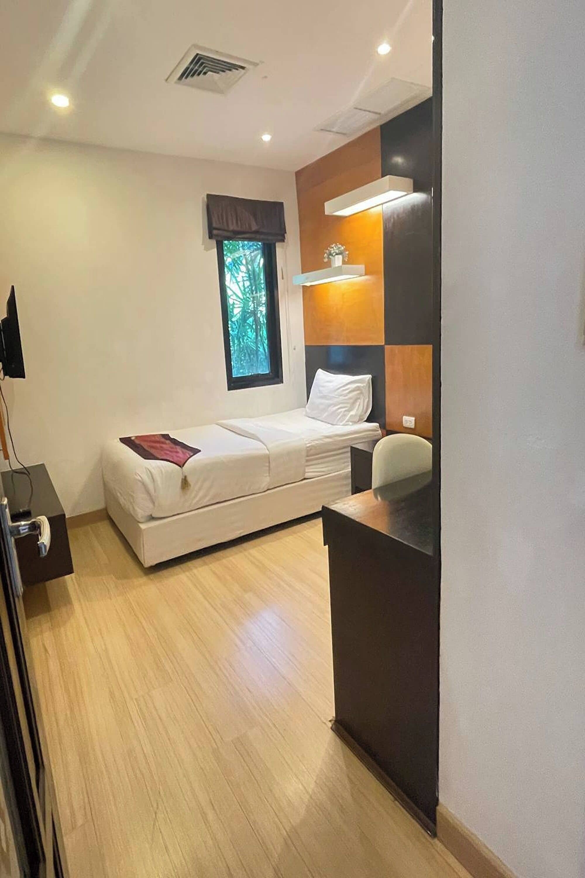 A compact hotel room with a bed, a desk, a chair, and a window with a view of greenery.
