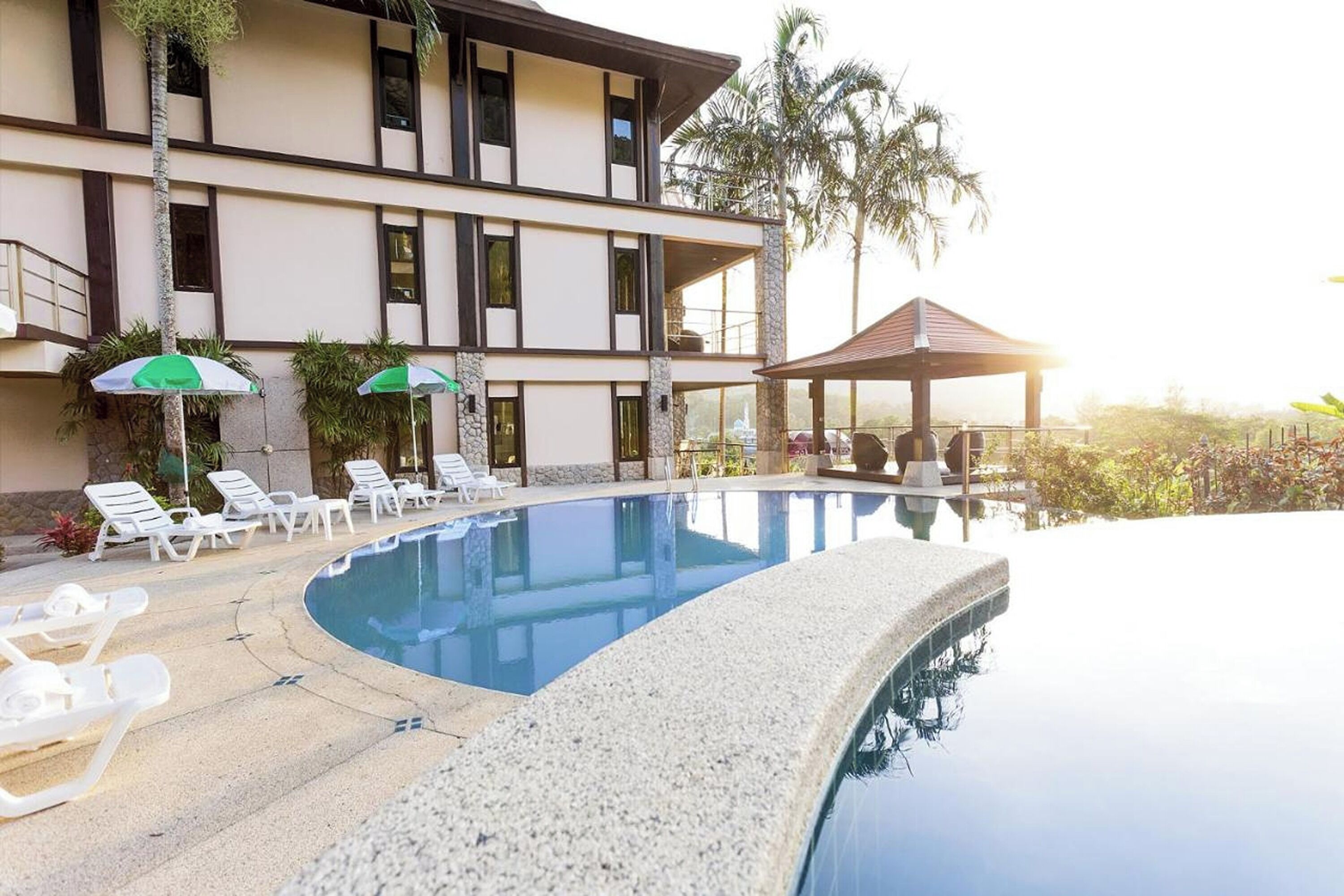 A pool area with lounge chairs, umbrellas, and a building with multiple floors and balconies.